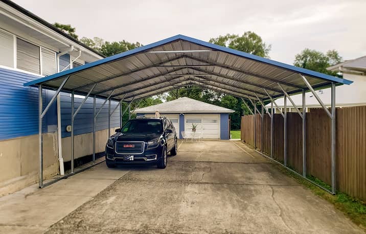 Red and tan metal carport with boxed-eave style roof covering red pickup truck