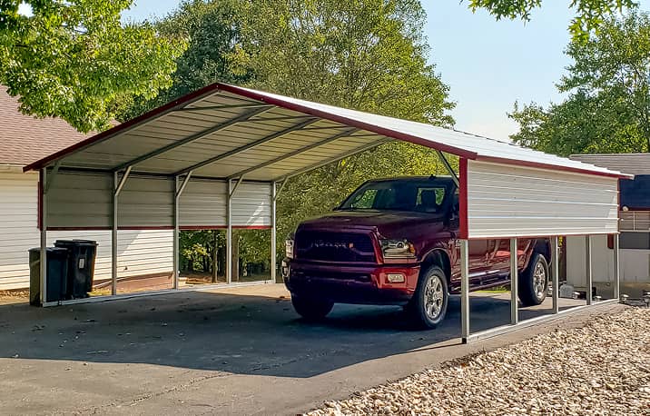 Green metal carport with boxed-eave style roof structure on gravel surface