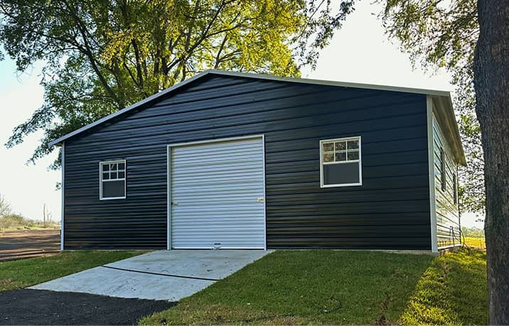 Dark blue boxed-eave style roof metal garage with overhead door and two windows on concrete pad