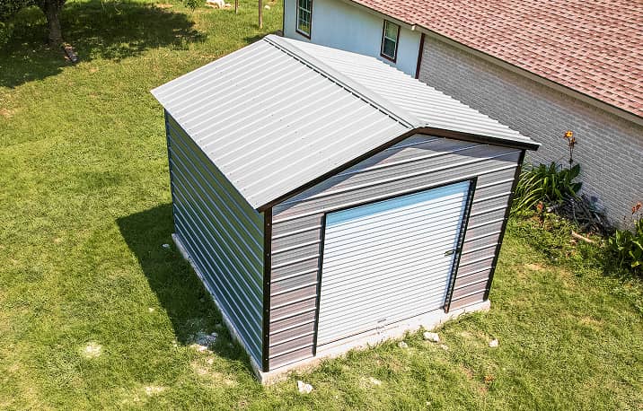 Gray vertical style roof metal garage building with white door on concrete pad
