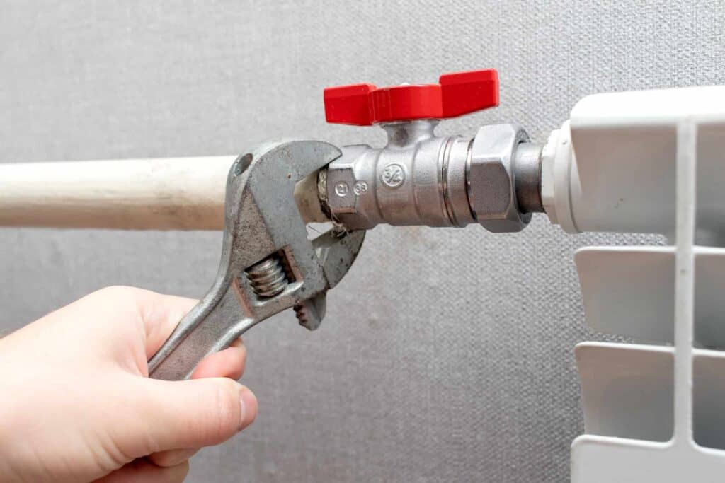 Adjustable wrench tightening a pipe fitting with a red valve.