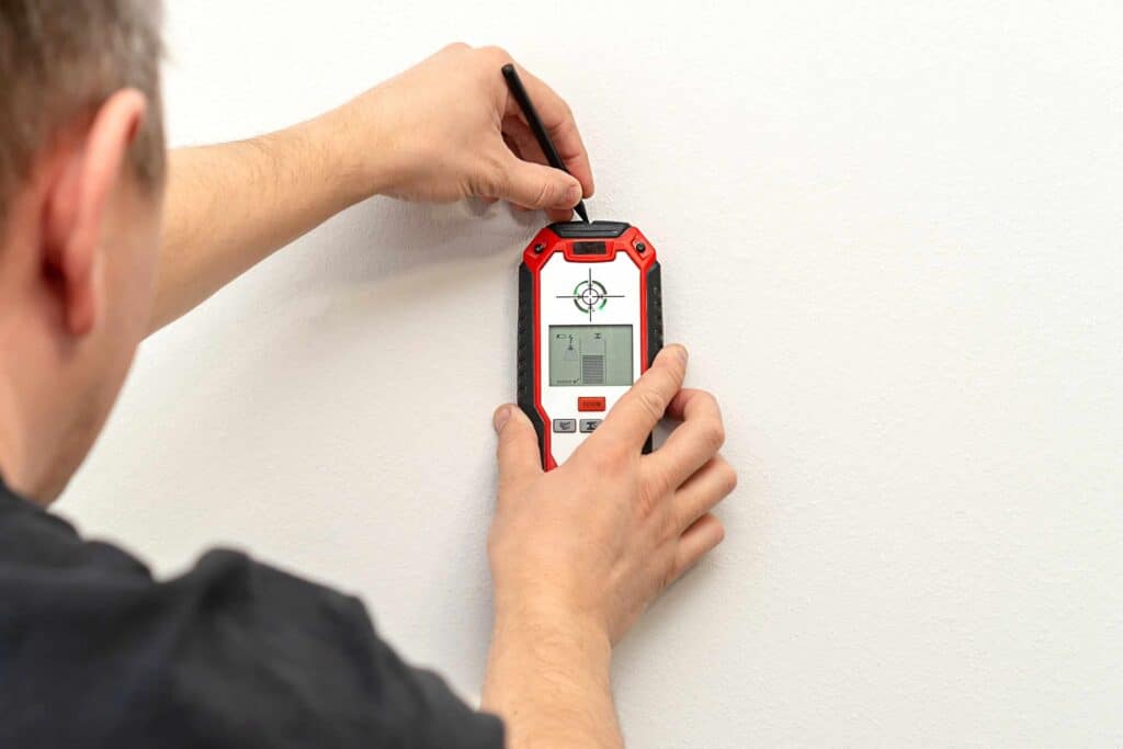 Man using a stud finder to locate studs in a wall.
