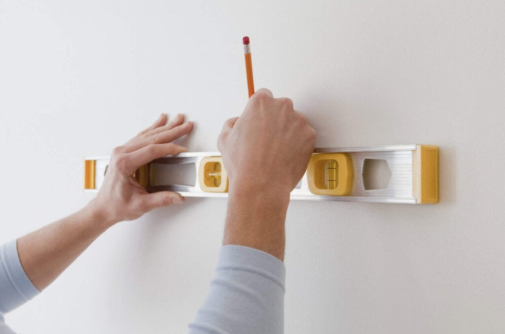 Man marking wall with pencil using a bubble level.