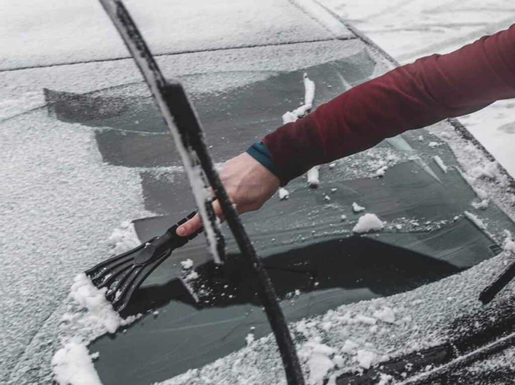 Man scraping snow and ice from a car windscreen.