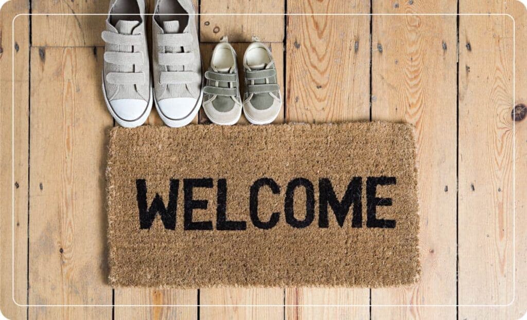 A welcome mat that says "Welcome" with two pairs of shoes off to the side.