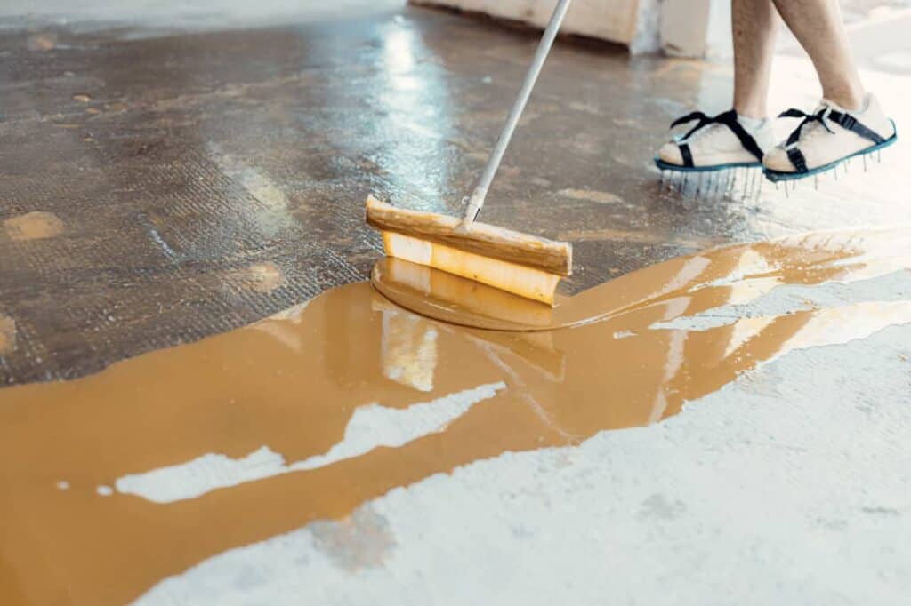 Someone spreads brown sealer across the floor of a garage.