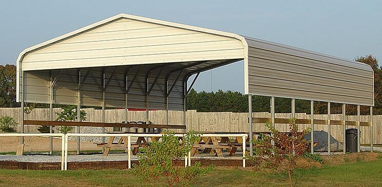 A partially enclosed beige metal carport with picnic tables underneath