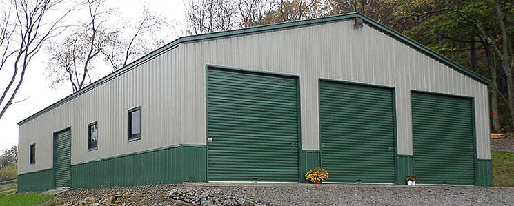 A tan metal building with green garage doors and trim