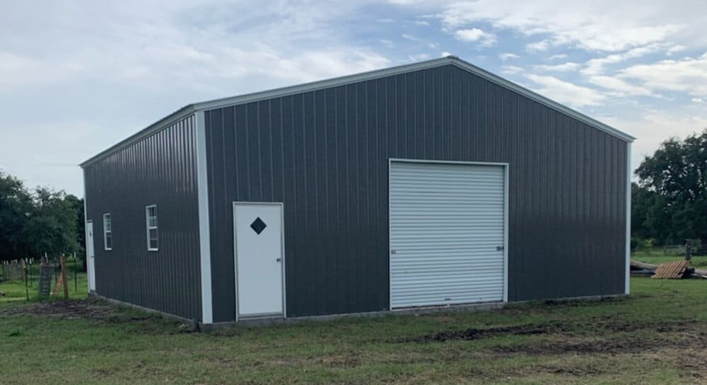 A dark-gray steel shop building with white doors and trim