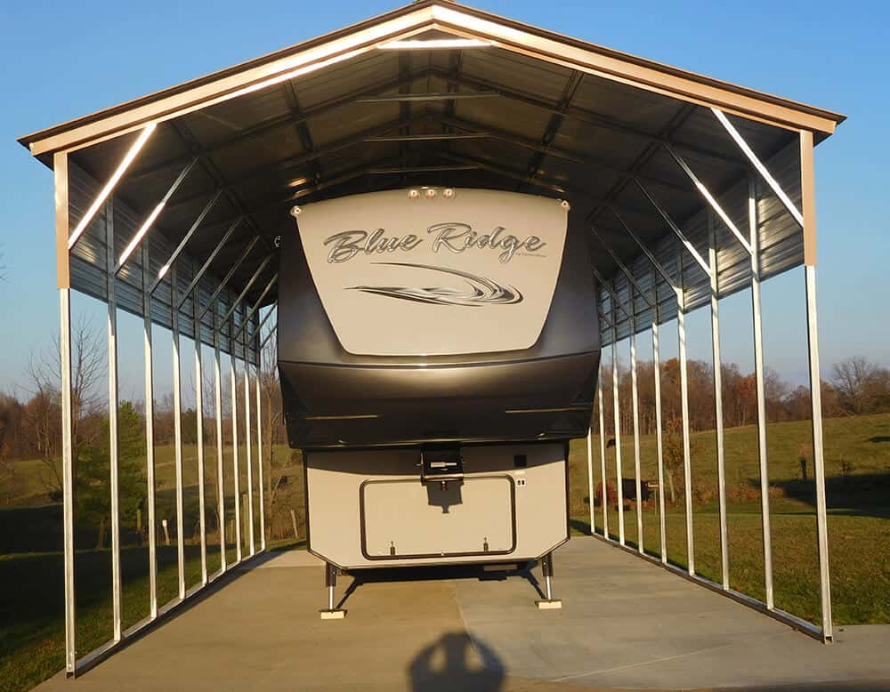 A travel trailer stands under a metal RV carport with optional side panels