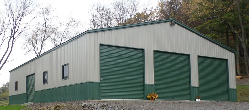 A large, tan prefab steel building with three green garage doors and green trim