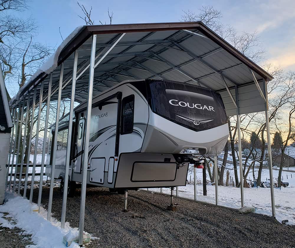 An RV is protected from the snow by a metal trailer cover