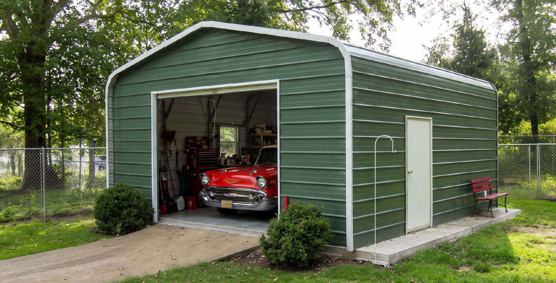 A green metal single-car garage with an open roll-up door revealing a red car parked inside, surrounded by shrubs and trees.
