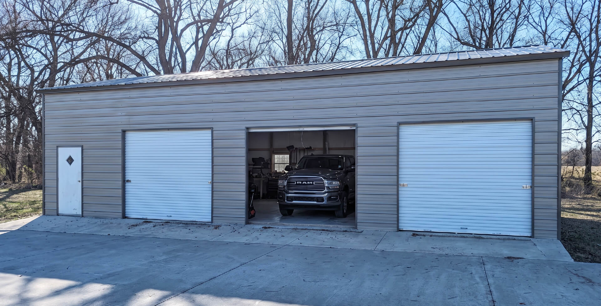 A gray three-car detached garage with two closed roll-up doors and an open center bay showing a dark car parked inside.