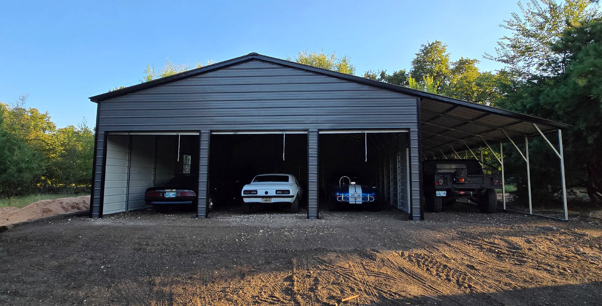 A gray three-car detached garage with two closed roll-up doors and an open center bay showing a dark car parked inside.
