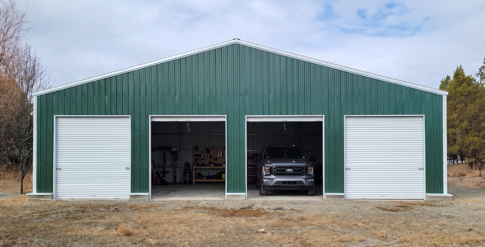 A large green and white four-car metal garage with a gabled roof, two closed white doors and two open bays with a dark car parked inside.