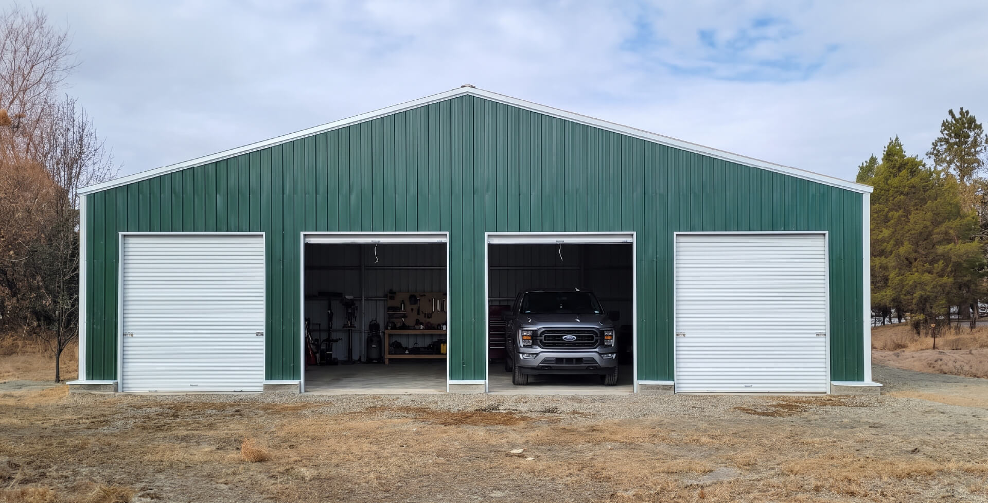 A large green and white four-car metal garage with a gabled roof, two closed white doors and two open bays with a dark car parked inside.
