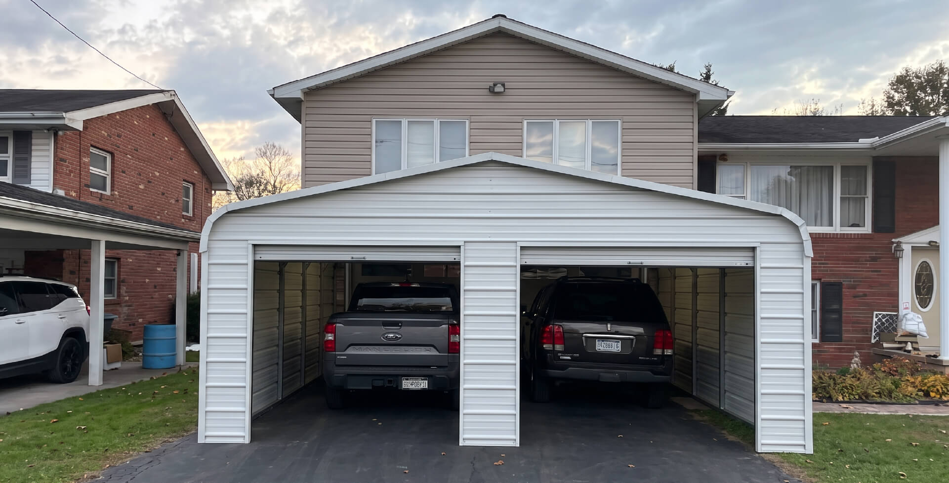 White attached two-car metal garage with open bays and vehicles parked inside