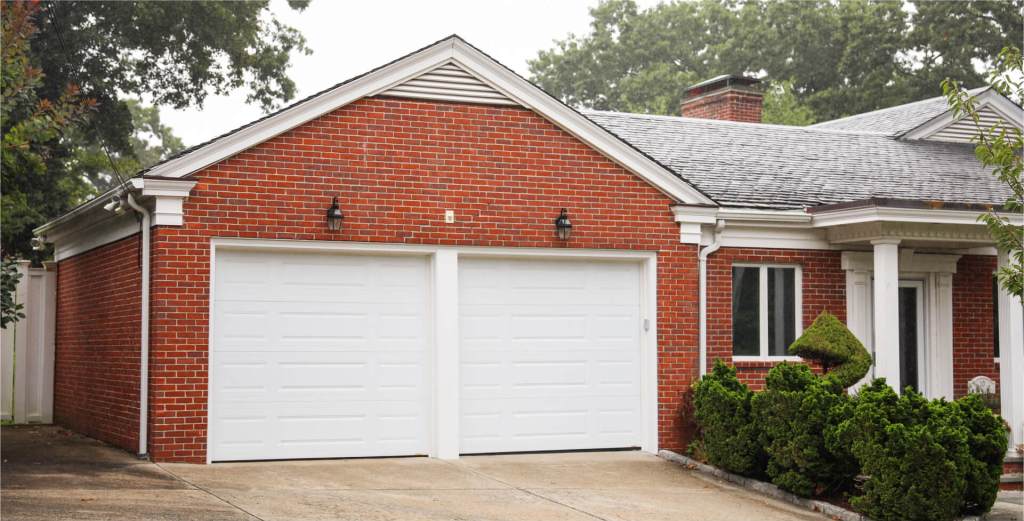 Brick garage with two white garage doors attached to a house.