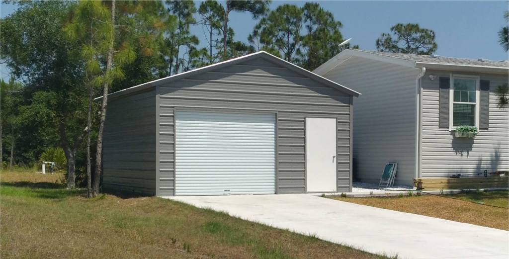 Gray metal garage with roll-up door and side door beside a house