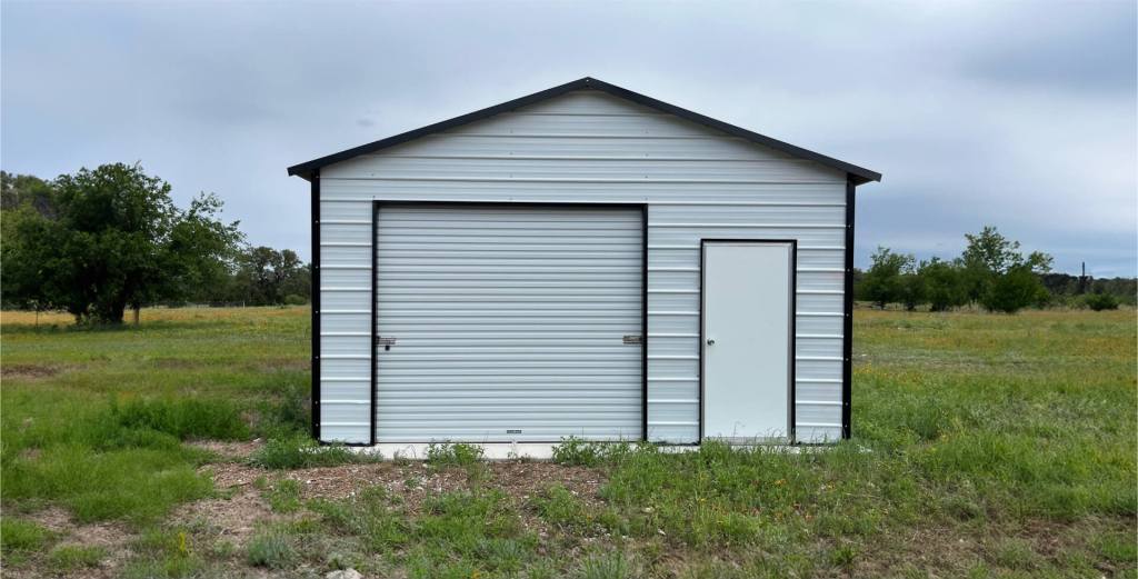 White metal garage with black trim, roll-up door, and side door in a rural setting