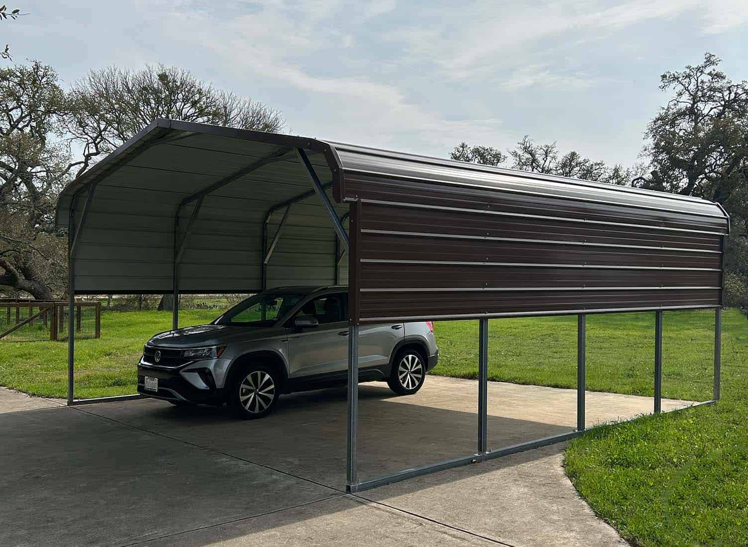 Photo of an SUV parked under a metal carport with partial wall panels. 