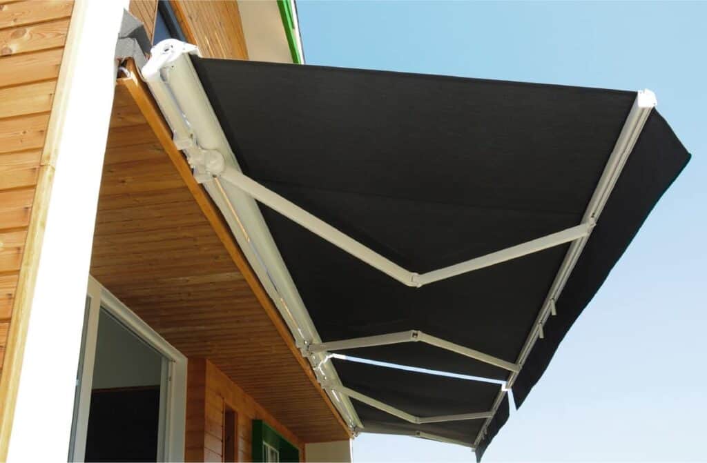 A retractable awning extends from the side of a wooden house with white trim.