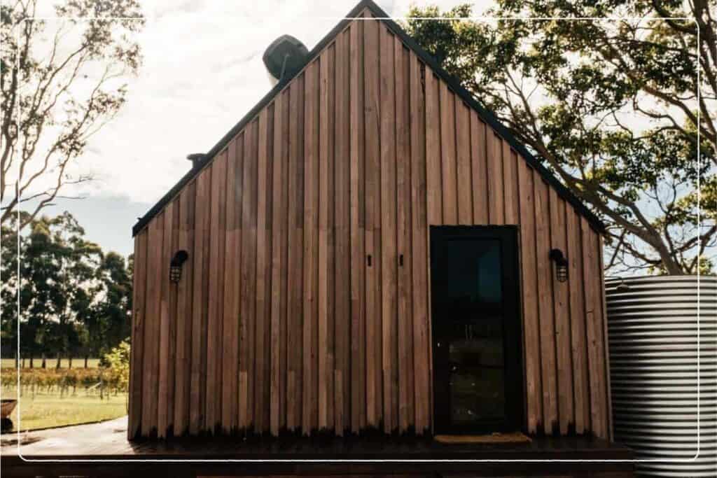 A small wooden barndominium with a metal rain tank outside.