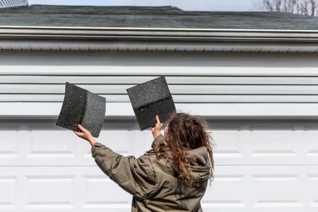 woman holding asphalt shingles in front of roof