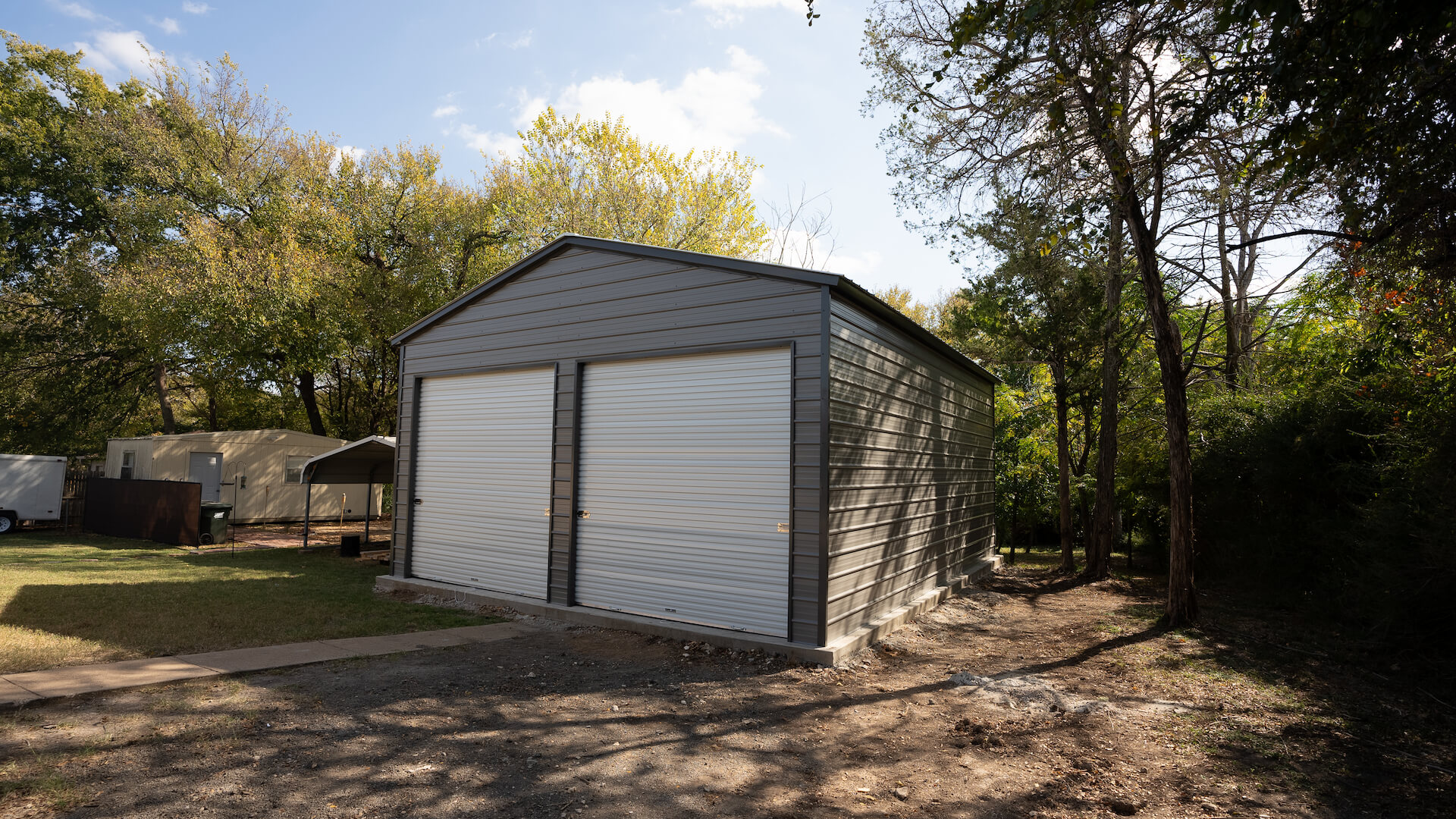 Dark gray 24-by-30-foot metal garage with two white roll-up doors on a wooded property.