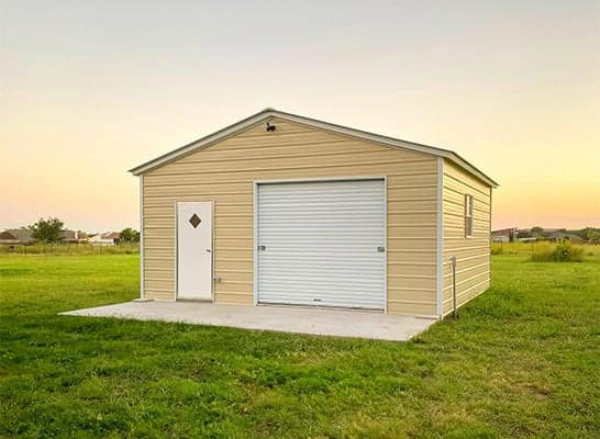 A pale yellow metal building with a large garage door in front of the sunset.