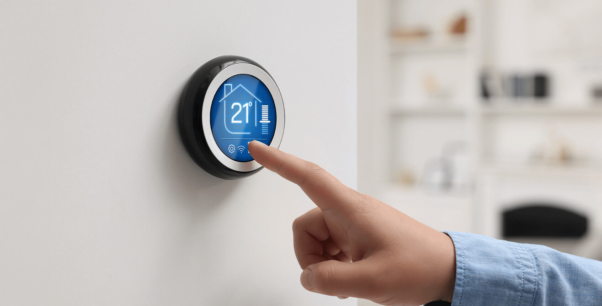 A hand presses a round smart thermostat mounted on a wall, displaying a temperature of 21°C in a modern home interior.