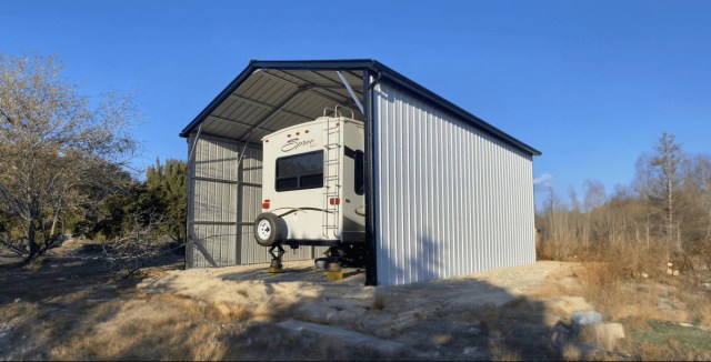 Enclosed metal RV carport with an open front, sheltering a fifth-wheel camper