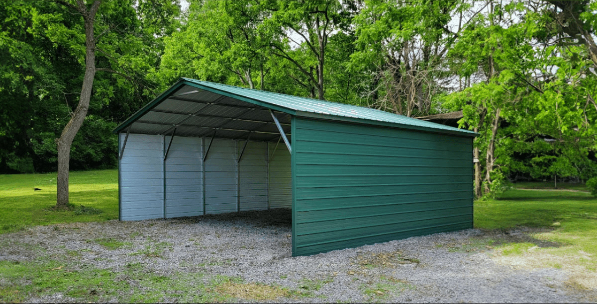 Enclosed green metal carport with open front, set on a gravel base in a wooded area.