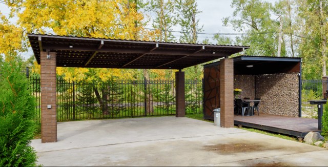 Open brick carport with a metal roof, next to a covered patio area with outdoor seating