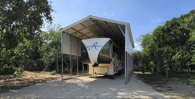 Large metal RV carport with side panels, sheltering a fifth-wheel camper on a gravel base