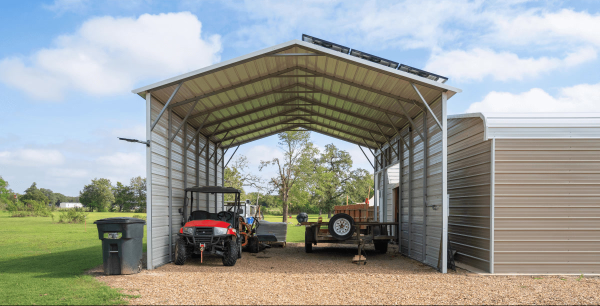 Metal carport with side panels, sheltering an ATV and a utility trailer on a gravel surface