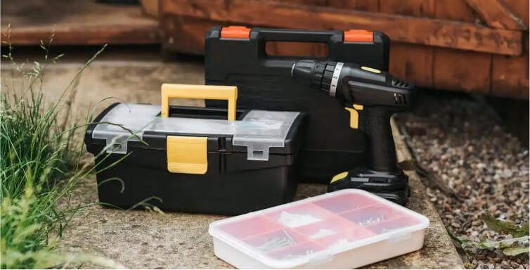 Set of toolboxes and a cordless drill placed outdoors on a paved surface