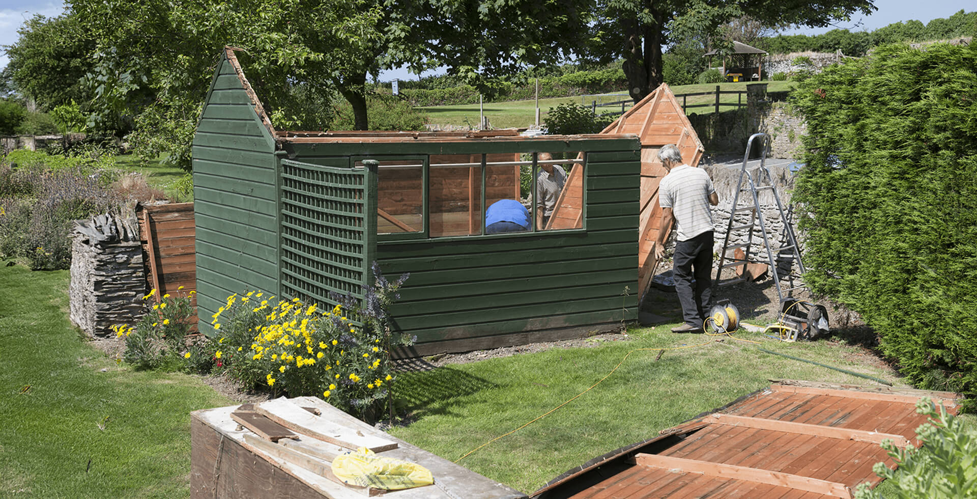Contractors dismantling a wooden garden shed during shed removal and demolition, with roof panels removed and tools on-site in a residential yard.