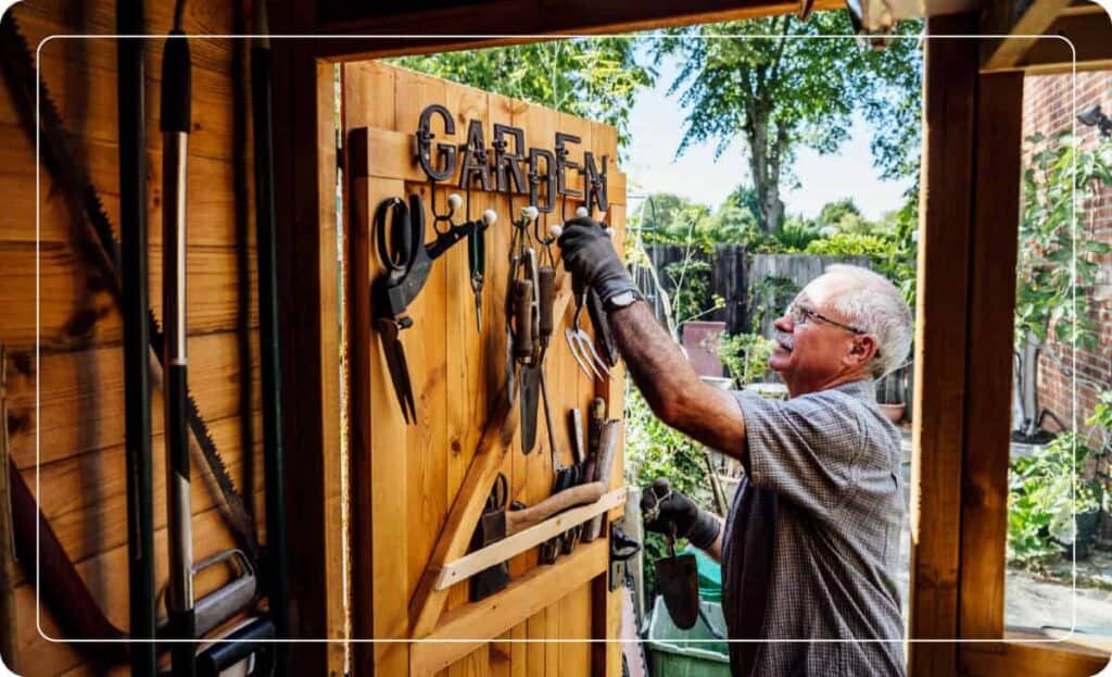 man grabbing garden tools from utility hooks on shed
