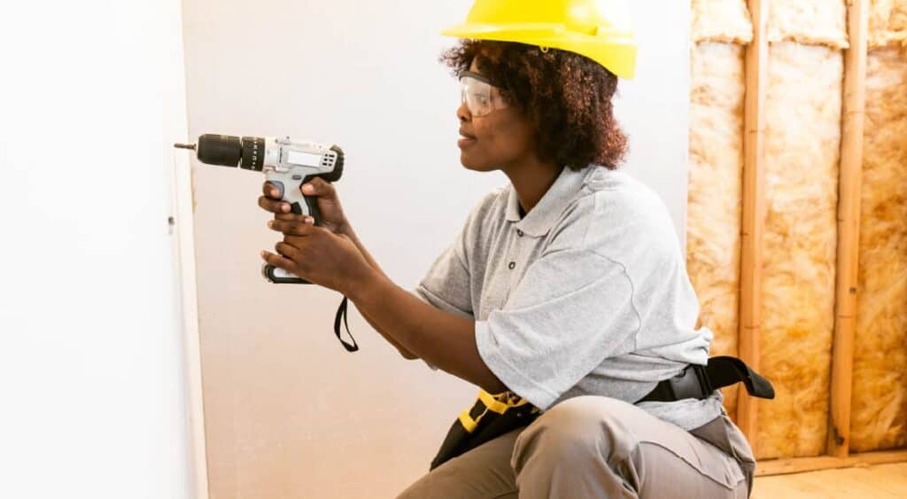 A woman uses a power driver to secure drywall over the insulated garage frame. 