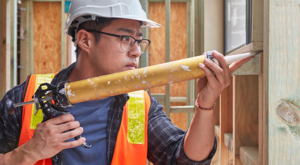 A contractor applies caulk between the garage frame and a window. 