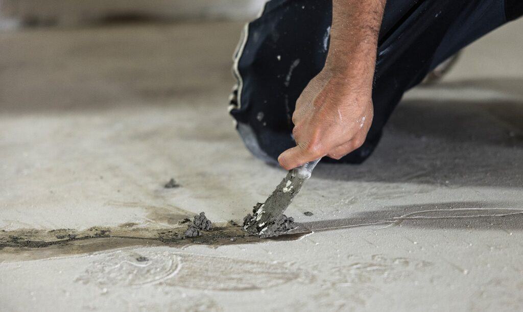 person applying concrete crack filler to garage floor