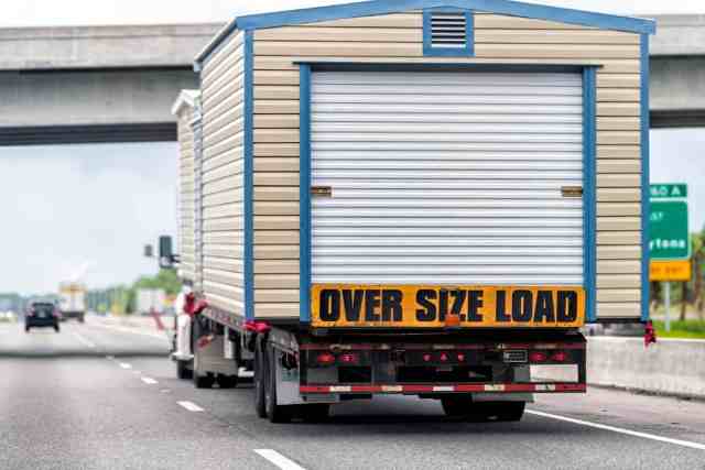 Truck moving large sheds on a flatbed trailer