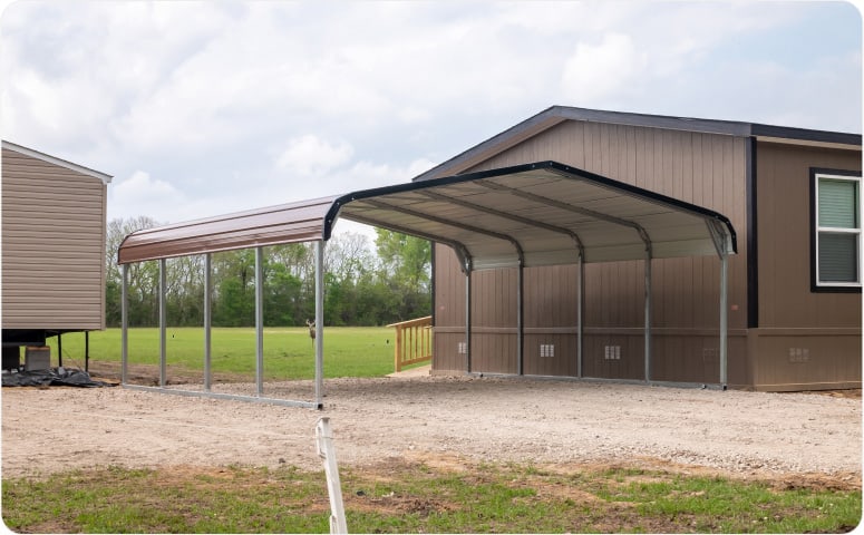 A metal carport on a dirt road next to a building