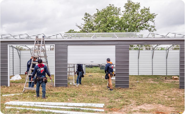 A construction crew building a large metal carport that is fully enclosed with siding and garage doors