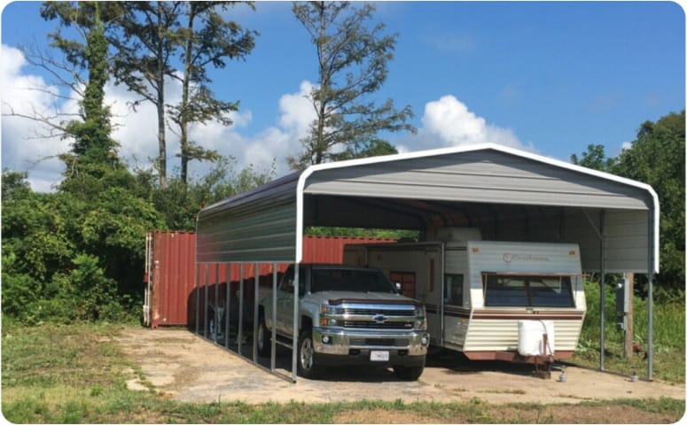 A partially enclosed metal carport with a truck and a fifth wheel parked inside