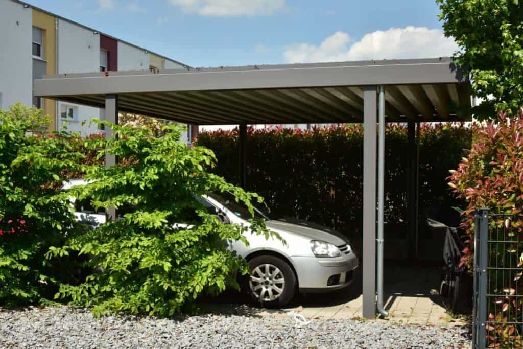 car parked beneath metal carport surrounded by plants