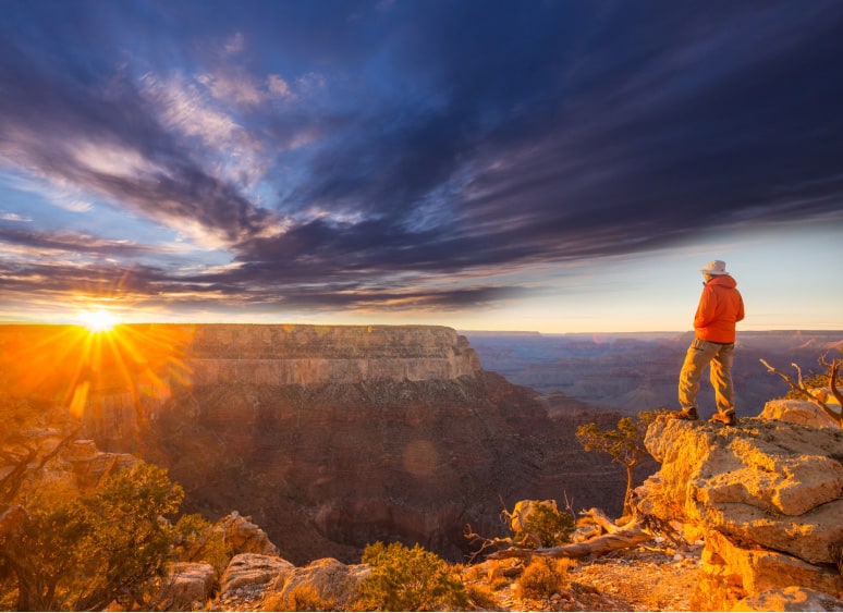 A person standing on a rock watching the sunset over a canyon.
