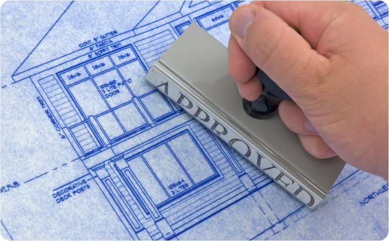 A rubber stamp with the word "approved" being applied to building blueprints.